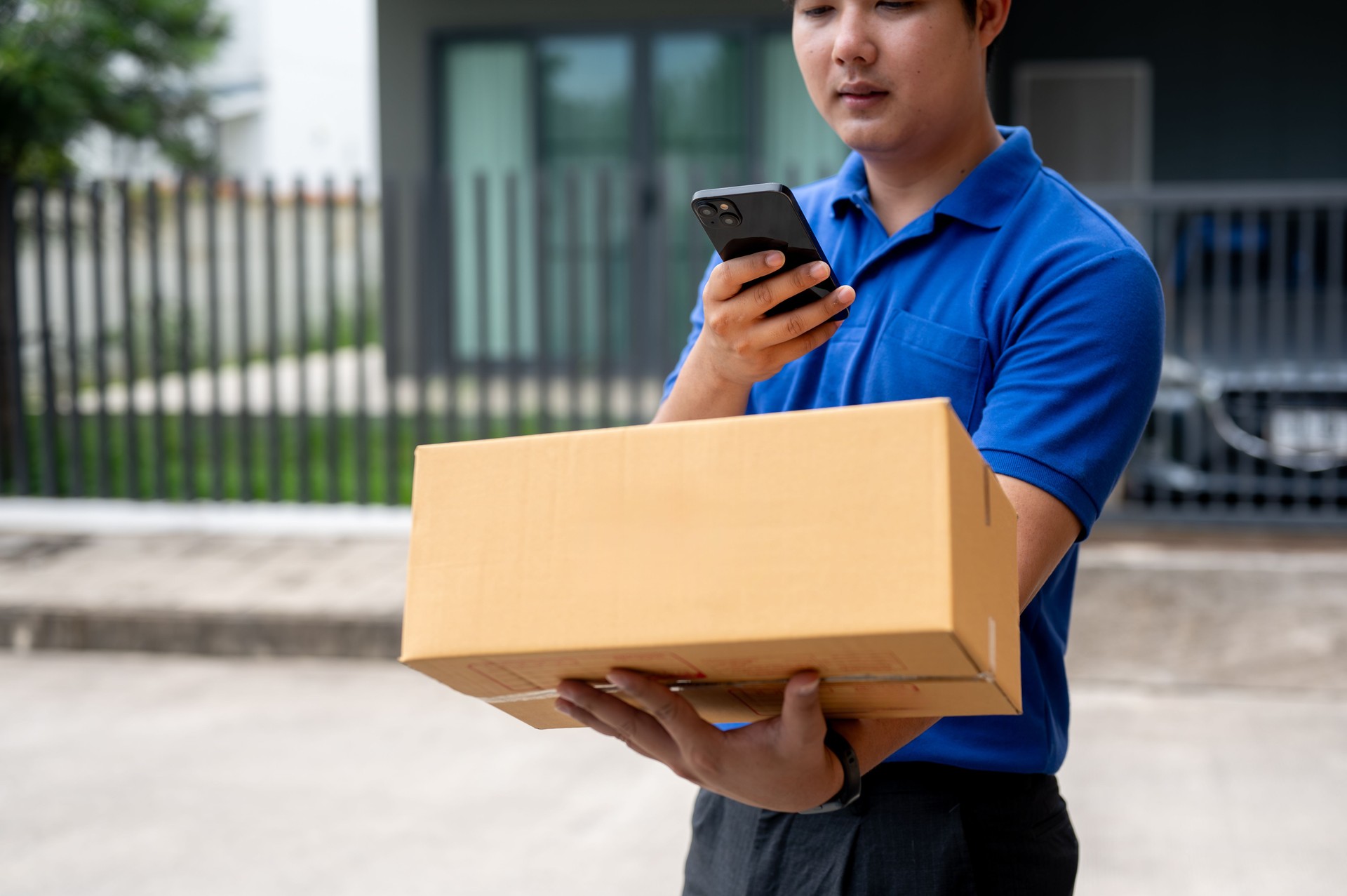 A delivery guy is taking a picture of a package before delivering it in front of a customer's house.